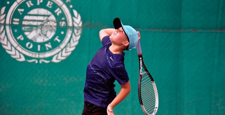 child on tennis court at The Club at Harper's Point holding racquet behind head in motion to hit tennis ball
