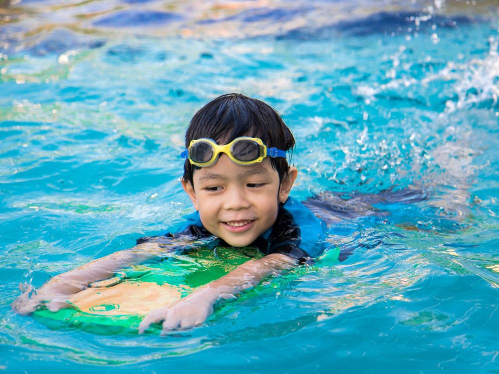 a junior swimmer practices feet kicking in an outdoor pool at the club at harpers point during junior swim lessons